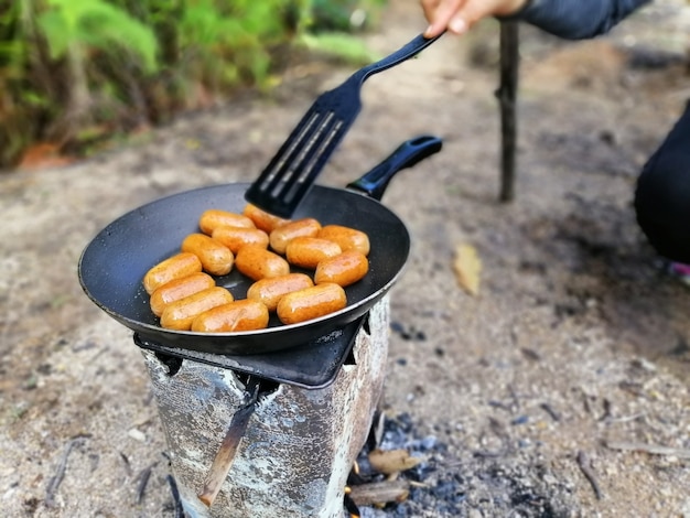 Vuur heerlijke worstjes koken in een pan boven kampvuur. zomerpicknick.