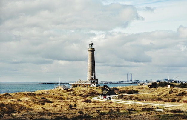Vuurtoren aan wal bij de zee tegen bewolkte lucht