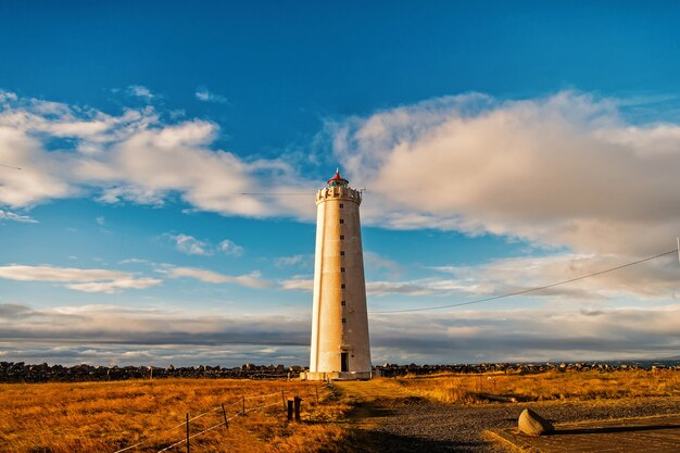 Vuurtoren in reykjavik, ijsland. Vuurtorentoren in herfst veld op bewolkte blauwe hemel. Structuur en ontwerp. Navigatiehulpconcept.