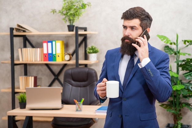 Wacht even Serieuze man zit aan de telefoon en drinkt koffie Telefoongesprek op het werk Zakelijk gesprek Mobiele communicatie