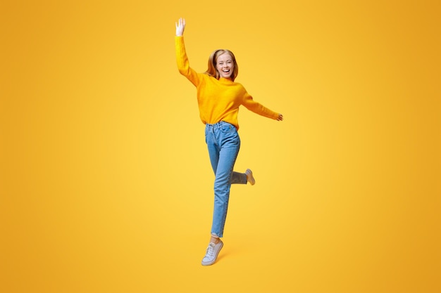 Wacht op me positieve tienermeisje loopt op de lucht over oranje studio achtergrond