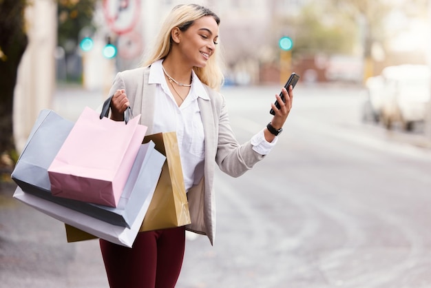 Wachten op haar rit. Bijgesneden opname van een aantrekkelijke jonge vrouw die haar mobiele telefoon checkt om te zien waar haar taxi is terwijl ze aan het winkelen is in de stad.