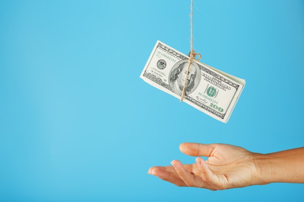 A wad of dollars on string above a human palm on blue.