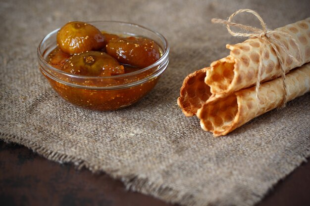 Wafelbroodjes vastgebonden met touw en vijgenjam in een glazen kom op jute en op donker aanrecht