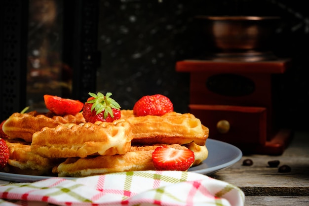 Wafels met aardbeien en honingzoete gebakjes op plaat tegen achtergrondkoffiemolen en decoratieve lamp met kaars