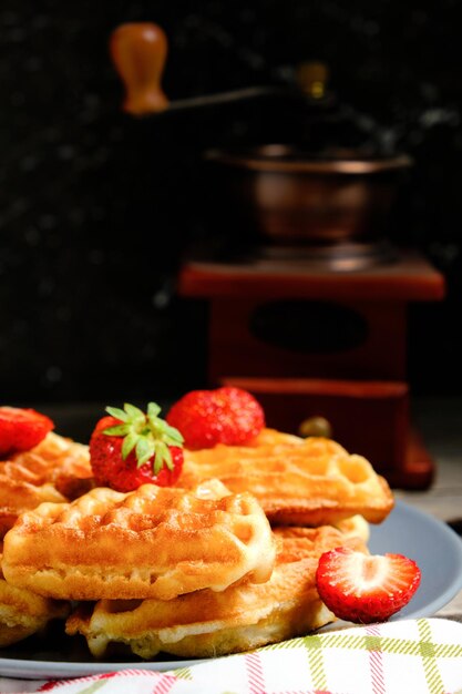 Wafels met aardbeien en honingzoete gebakjes op plaat tegen achtergrondkoffiemolen