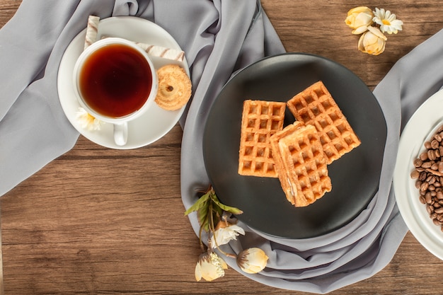 Wafels op een zwarte schotel en een kopje thee.