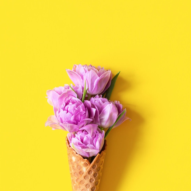 Wafer cone with tulips on yellow background Flower ice cream spring concept with first flowers