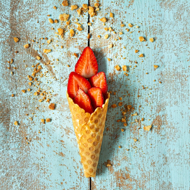 Wafer cones for ice cream with ripe strawberries on blue background Summer food
