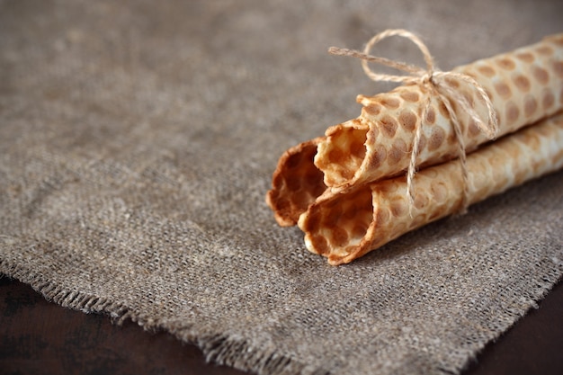 Wafer rolls are hollow without filling twine tied on the grey sackcloth and a dark countertop. Sweet confectionery.