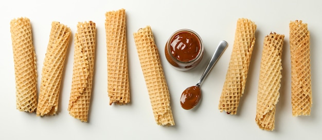 Wafer rolls and jar with condensed milk on white background