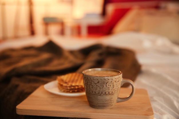 Wafers and cup of hot drink on cozy double bed