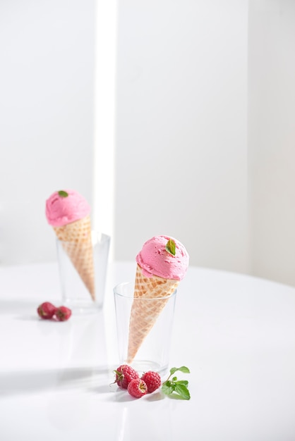 Waffle cone filled with fresh raspberry ice cream in glass cup with fresh raspberry sitting on tabletop