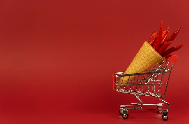 A waffle cone full of red hot chili peppers lies in a shopping trolley on a red background