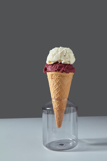 Waffle cone stands in a glass jar with cherry and white milk dessert on a gray wall on the kitchen table. Summer concept.