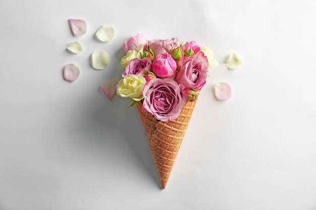 Waffle cone with bouquet of beautiful roses on white background