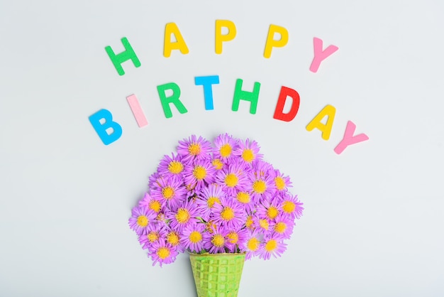 Foto cono di cialda con fiori aster alpino su sfondo bianco, testo di buon compleanno. piatto, vista dall'alto