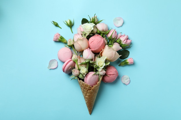 Waffle cone with flowers, ice cream balls and macaroons on blue background