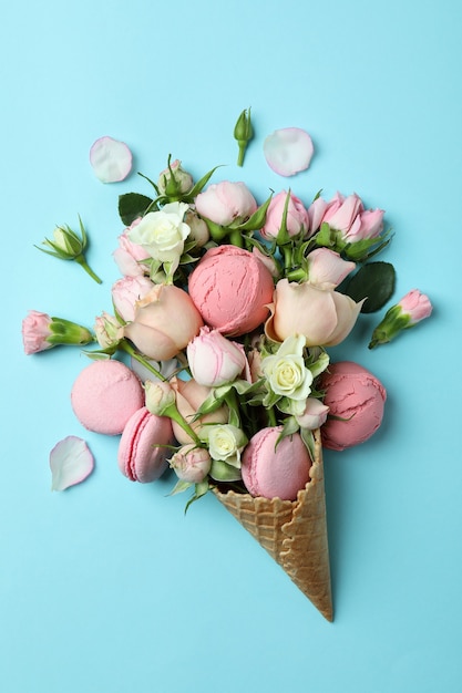 Waffle cone with flowers, ice cream balls and macaroons on blue background