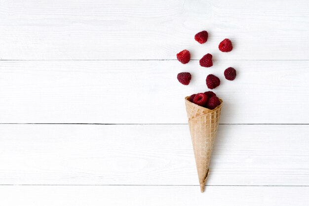Waffle cone with fresh organic raspberry berries on white wooden background with copy space