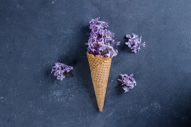 Waffle cone with purple lilac on dark blue stone concrete table background. Flat-lay, top view