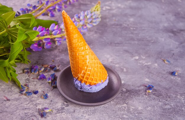 Waffle cone with purple lilac ice cream on the dark gray surface decorating lupins