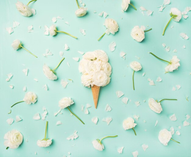 Waffle cone with white buttercup flowers over light blue background