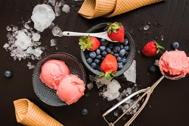 Waffle cones near fresh berries and ice cream on dishes and spoon among ice