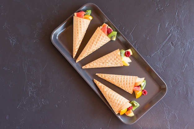 Waffle cones with fresh fruit on a black tray. top view. delicious dessert.