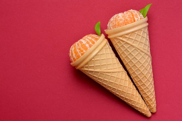 Waffle cones with ripe tangerines on a red background copy space