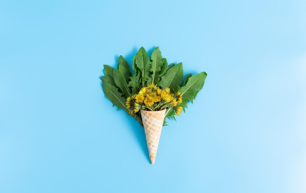Waffle cup with a bouquet of dandelion and leaves on a blue background