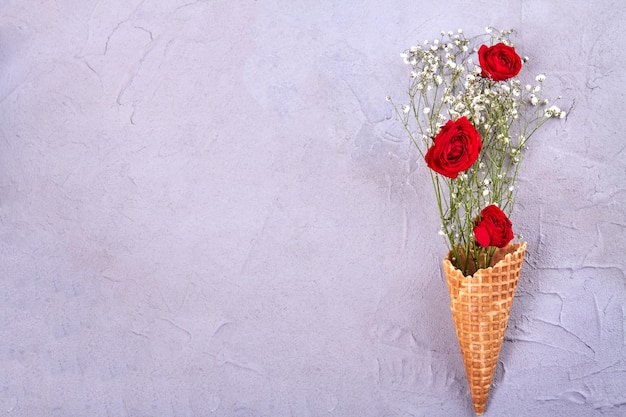 Waffle ice cream cone with flowers and copy space red roses and tiny white flowers