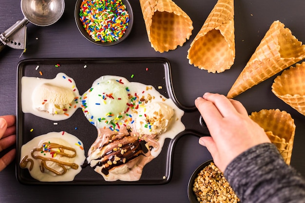 Waffle ice cream cones with plate of ice cream scoops on a black cutting board.