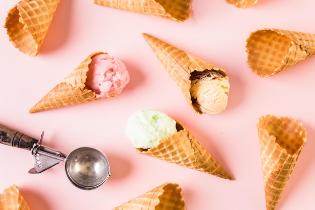 Waffle ice cream cones with plate of ice cream scoops on a pink background.
