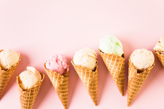 Вафельные рожки мороженого с тарелкой совков мороженого на розовом фоне.