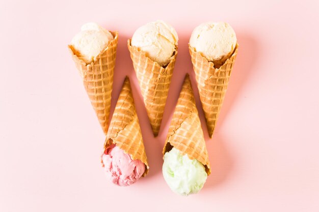 Waffle ice cream cones with plate of ice cream scoops on a pink background.