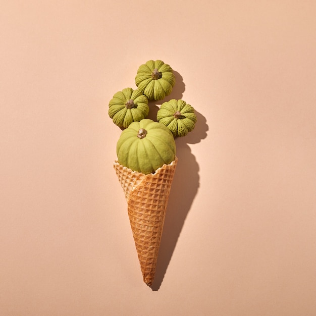 Cono gelato di cialda con zucche verdi su fondo crema.