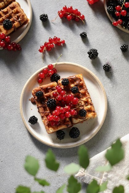 A waffle with berries on it sits on a plate with a spoon.