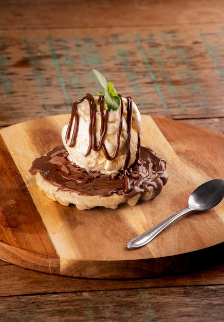 Waffle with chocolate and hazelnut cream and a scoop of vanilla ice cream on a round wooden board with dessert spoon angle view