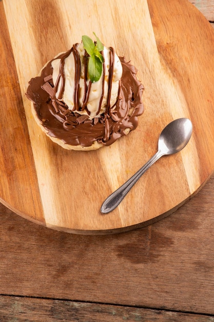 Waffle with chocolate and hazelnut cream and a scoop of vanilla ice cream on round wooden board with dessert spoon top view closeup