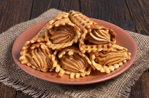 Waffles cones with boiled condensed milk in plate on dark wooden table