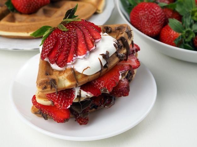 Waffles decorated with strawberries chocolate and whipped cream on white background