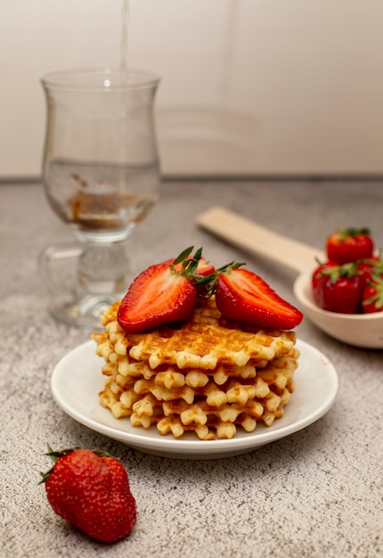 Waffles served with strawberries on a white cutting board on a gray table and a basket with ripe str