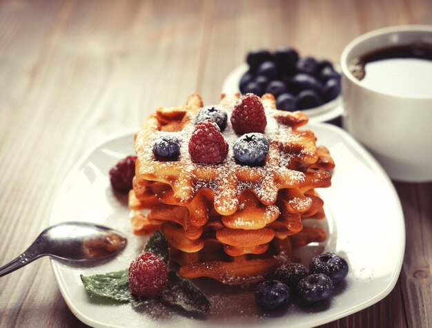 Waffles with berries on a white plate and coffee close up