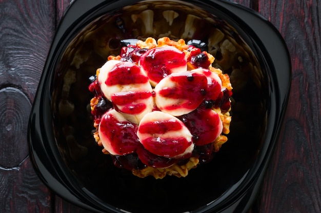 Waffles with blueberry jam and banana slices on a black plate close up