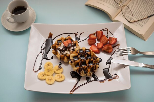 Waffles with chocolate fruits a cup of coffee and a book on a blue background