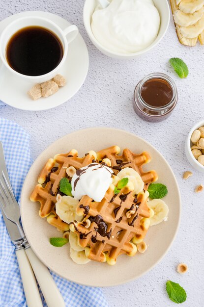 Waffles with fresh banana, hazelnuts, chocolate sauce and whipped cream on a plate