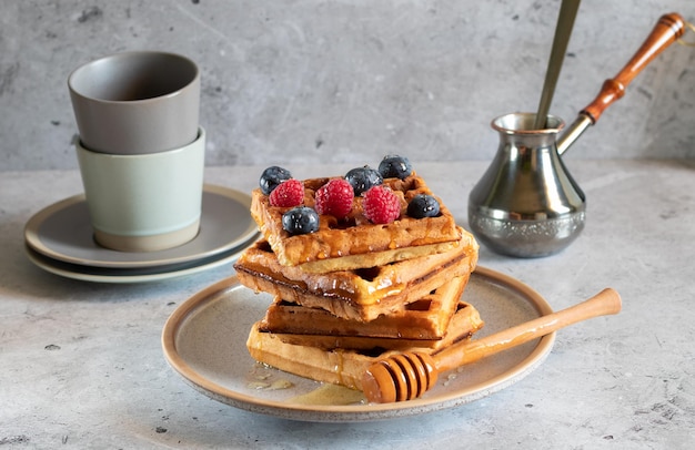 Waffles with fresh berries honey jezva and cups on a light concrete background Side view horizontal