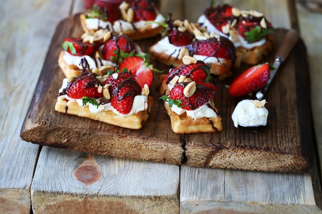 Waffles with fresh strawberries cream cheese and chocolate on a wooden board