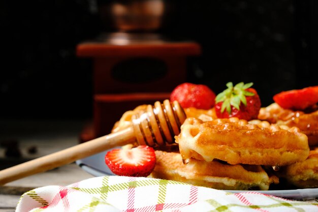 Waffles with strawberries and honey sweet pastries on plate against background coffee grinder